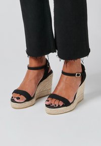 Zwarte wedge-sandalen met enkelbandjes. Heeft een jute-beklede hak en een gladde suède bovenkant. Het open teenontwerp toont gepolijste teennagels.