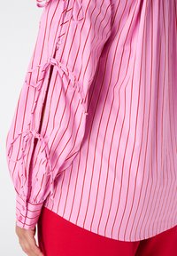 Roze shirt met lange mouwen, voorzien van verticale rode strepen, geraffineerde mouwen met strikdetails en een gebogen zoom.