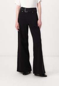 Zwarte wijde broek met hoge taille, voorzien van een riem met een zilveren gesp en twee achterzakken. Gemaakt van een gestructureerde stof.