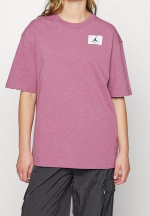 Lyserød t-shirt med korte ærmer lavet af bomuld, med en lille hvid etiket med et sort logo. Kombineret med mørke, teksturerede cargobukser.