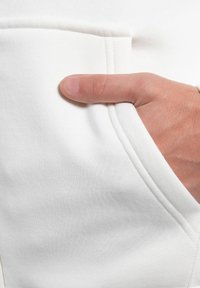 Primo piano di un tessuto di felpa bianca, con una tasca cucita e una mano che riposa all'interno. Texture morbida con una finitura liscia.