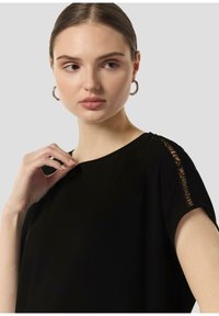 Black short-sleeve top with a subtle lace detail on the shoulder. Made of a smooth, lightweight fabric. Minimalist design.
