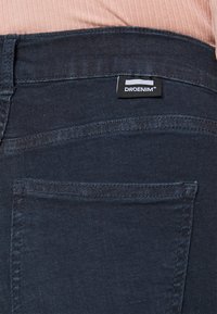 Vaqueros de mezclilla azul oscuro con una textura suave, que cuentan con bolsillos traseros y una etiqueta negra de DRDENIM en la cintura.