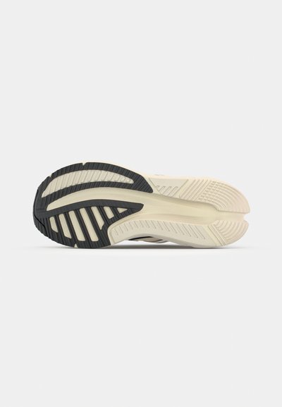 Suela de zapatilla negra y crema con patrones texturizados, forma acampanada y ranuras distintivas para tracción. Material de goma con flexibilidad.