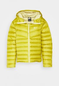 Keltainen vuorattu takki hupulla, jossa on vaakasuora ompelu, edessä vetoketju ja pieni valkoinen logo vasemmassa rinnassa.