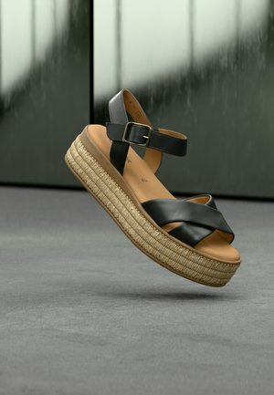 Musta nahkainen kiilakorkosandaali ristikkäisillä remmeillä, säädettävällä nilkkahihnalla ja luonnollisella punotulla juuttipohjalla, kohotettu muotoilu sileällä viimeistelyllä.