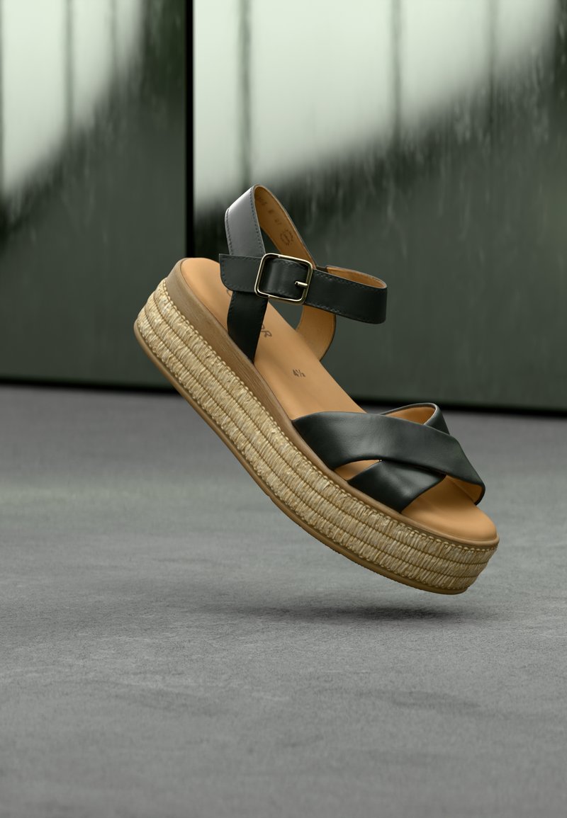 Sandale compensée en cuir noir avec brides croisées, boucle réglable à la cheville, semelle en jute tissée naturelle, design surélevé avec une finition lisse.