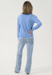 Ljusblå stickad tröja med långa ärmar, med ribbat nederkant och detalj längs ryggen, tillsammans med ljusblå utsvängda jeans med kontrasterande sömmar.