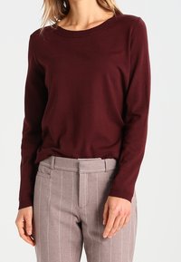 Haut en maille bordeaux à manches longues avec un col rond, associé à un pantalon gris clair à fines rayures, coupe fuselée et poches latérales.