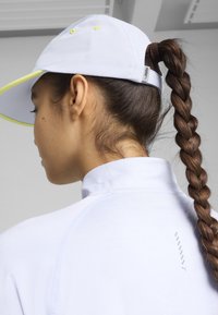 Gorra blanca con acentos en lima, diseño elegante y una coleta en la parte trasera. Camisa de textura suave con un detalle de logo en el cuello.