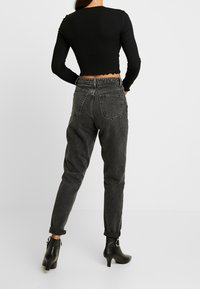 Schwarzes, geripptes Langarm-Crop-Top kombiniert mit hochgeschnittenen, grauen Jeans. Die Jeans haben einen lockeren Schnitt, umgekrempelte Säume und Gesäßtaschen.