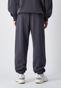 Pantalons de survêtement gris foncé avec des poignets élastiques aux chevilles, fabriqués en tissu doux, présentant une coupe décontractée et des poches latérales, associés à des baskets blanches.