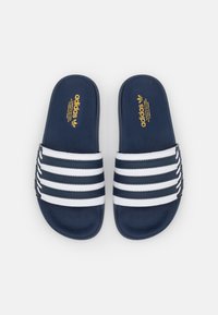Navy blue slide sandals with white striped band, featuring textured upper and golden logo detail. Soft material, open-toe design.