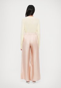 Helebeež kollane kootud topp, mida on kombineeritud lahtiste pastelse roosa siidist laiade pükstega. Omadusteks on voltidega vöökoht ja peen läige.