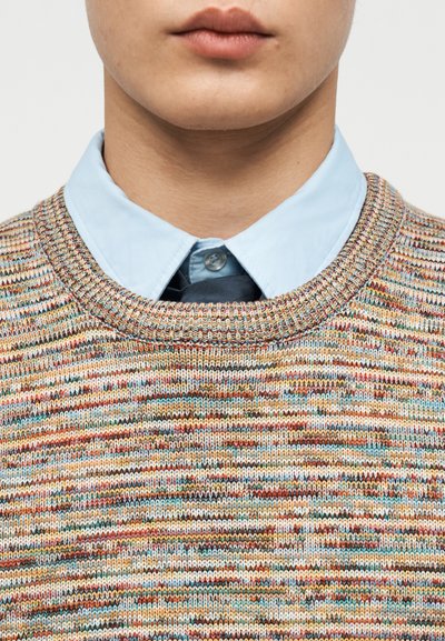Gros plan sur le cou et les lèvres portant un pull tricoté multicolore par-dessus une chemise bleu clair à col, avec une cravate sombre en dessous.