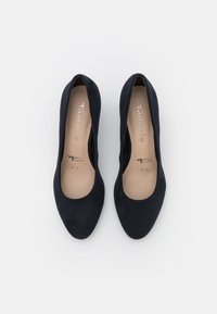 Zapatos de tacón cerrado de ante azul marino con una textura suave y un diseño redondeado. En el interior, una plantilla beige presenta el detalle de la marca y la talla.