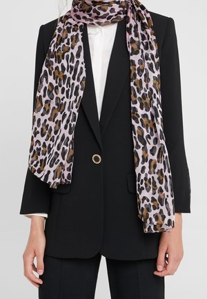 Femme portant un blazer noir avec un bouton doré, une chemise blanche et une écharpe rose à imprimé léopard drapée autour du cou et tombant sur le devant.