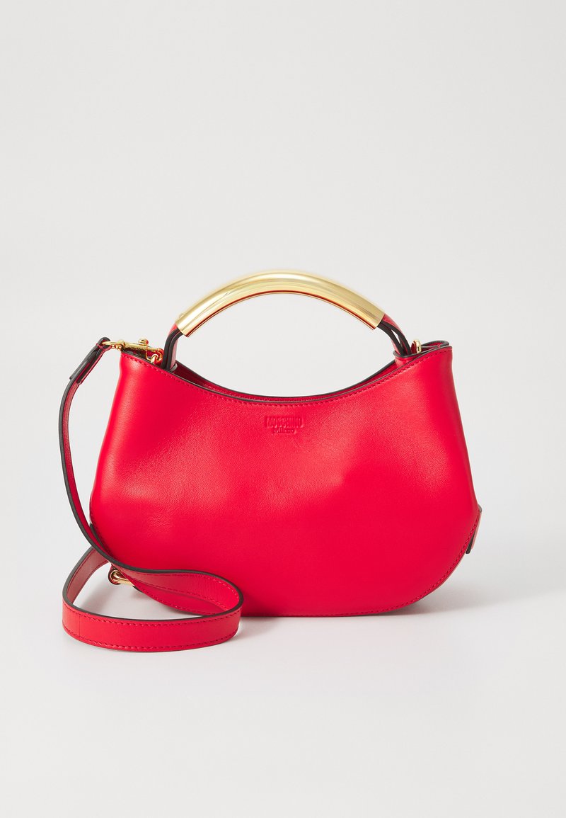 Punainen nahkainen käsilaukku, jossa on kaareva siluetti, kultainen metallikahva ja säädettävä olkahihna. Sileä pinta, jossa on minimaalinen brändäys.