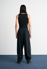 Débardeur noir côtelé porté avec un pantalon noir ample, présentant une taille élastique, des poches latérales et des bottes noires.