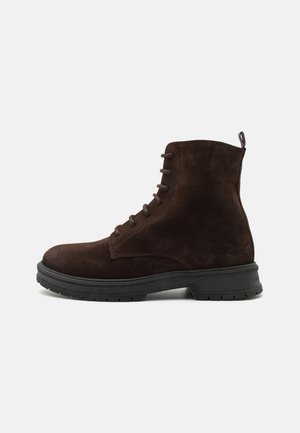 Stivale alla caviglia in suede marrone con punta tonda, design con lacci e suola in gomma nera testurizzata con un leggero tacco e linguetta per l'estrazione.