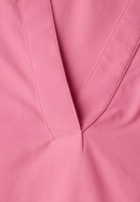 Rosa Stoff mit einem V-Ausschnitt, der mit Steppnähten versehen ist, und einer glatten Textur. Nahaufnahme des Designs des Kleidungsstücks.