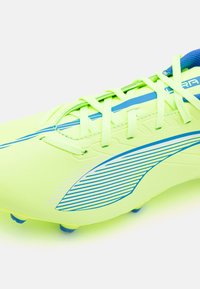 Crampons de football vert citron avec des accents bleus, dotés d'une surface texturée et d'un motif à rayures diagonales, conçus pour la performance sur l'herbe.