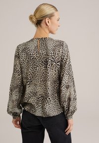 Blus med leopardmönster, avslappnad passform, långa puffärmar och en nyckelhålsknäppning vid ryggen. Tillverkad av mjukt, lätt material.