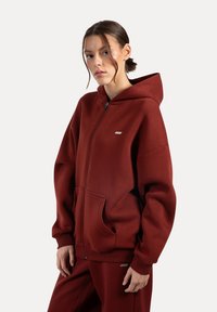 Bordowy hoodie z zamkiem błyskawicznym, wykonany z miękkiego materiału, z kieszenią typu kangur, ściągaczami na rękawach oraz małym logo na piersi.