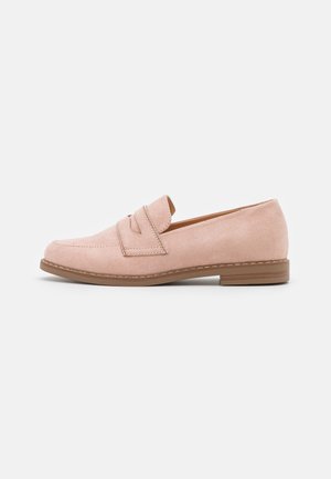 Mocassins en daim rose clair avec une semelle plate, dotés d'une bride décorative à l'avant et de détails de couture le long du bord. Texture lisse.