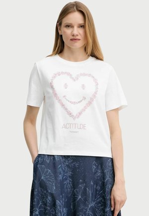 T-shirt bianca in cotone con maniche corte, caratterizzata da un design a forma di cuore floreale rosa e una faccina sorridente, abbinata a una gonna blu a fantasia.