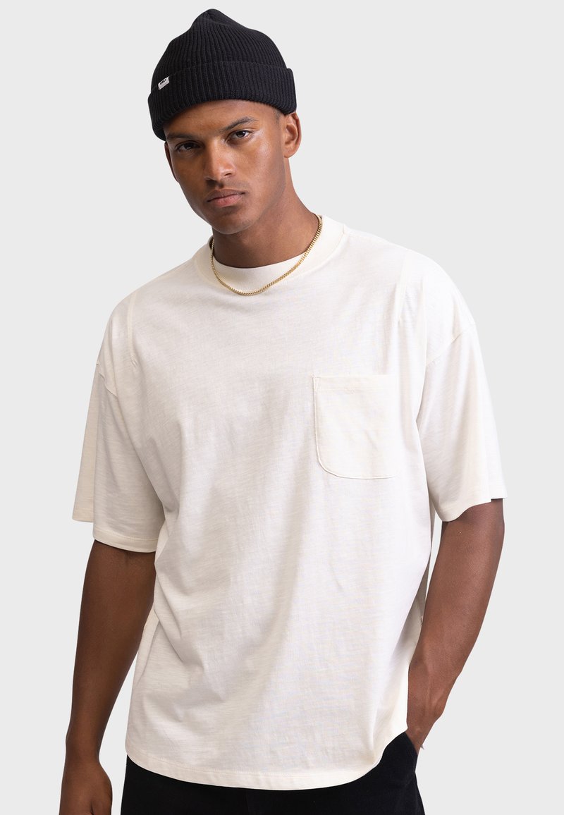 Relaxed-fit, light beige t-shirt with short sleeves, featuring a chest pocket. Smooth texture, cotton material, and a crew neckline.
