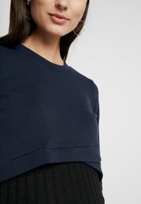 Sweater de gola redonda azul marinho em algodão suave com um design em camadas. Apresenta um corte ligeiramente solto e uma textura canelada na bainha.