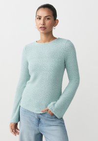 Hellblauer, weich strukturierter Pullover mit langen Ärmeln, rundem Ausschnitt und seitlichen Schlitzen, kombiniert mit Jeans aus Denim.