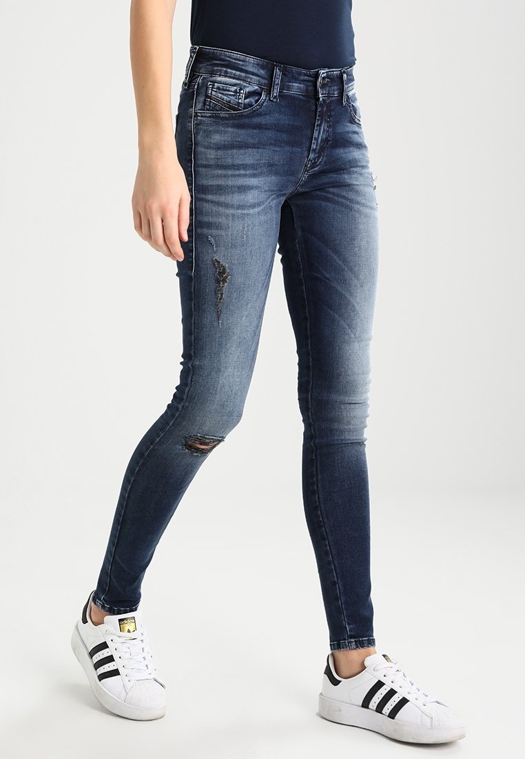 Blauwe skinny jeans van denim met vervaagde details en scheuren, gecombineerd met witte sneakers. De jeans hebben een klassiek vijf-pocket design.