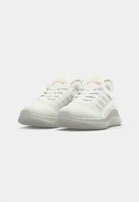 White mesh athletic shoes with textured soles, laces, and branded accents. Features a rounded toe and a cushioned sole design.