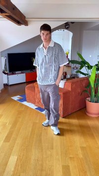 Hallikirjakeelne halli ja valge triibuline ülemõõduline polo särk koos kraega, kombinatsioonis heledate hallide cargo-pükstega ja valgete tossudega. Siseruum, millel on puidust põrand.