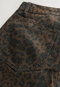 Gros plan d'une poche arrière sur un jean en denim marron avec un motif léopard noir et des coutures visibles.