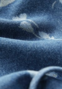 Denimriie sinine varjund, millel on peenet valget lillemustrit. Tekstuur on pehme, selgelt nähtava kudumisega ja õrnade voltidega.