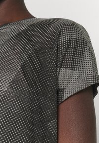 Close-up de la parte superior de la espalda y el hombro de una persona que lleva una camiseta negra y gris con un diseño geométrico punteado.