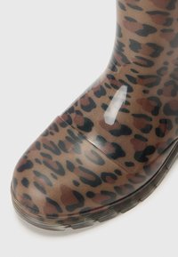 Botte en caoutchouc imprimée léopard avec une finition brillante, présentant un bout arrondi et une surface texturée. Principalement marron, avec des taches sombres et rouges.