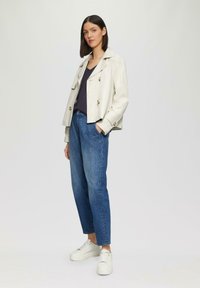Lichtbeige cropped jack met knopen aan de voorkant, gecombineerd met losse blauwe jeans en witte sneakers. Eenvoudig ontwerp met een casual pasvorm.