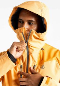 Orangene wasserdichte Jacke mit hohem Kragen, verstellbarer Kapuze, grauen Reißverschlüssen und Logodetail. Verfügt über Handreißverschlüsse und eine glatte Textur.