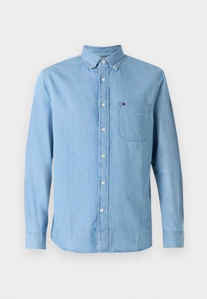 Chemise en denim bleu clair à boutons, avec un col, des manches longues et une poche poitrine. Elle présente un petit logo sur la poche.