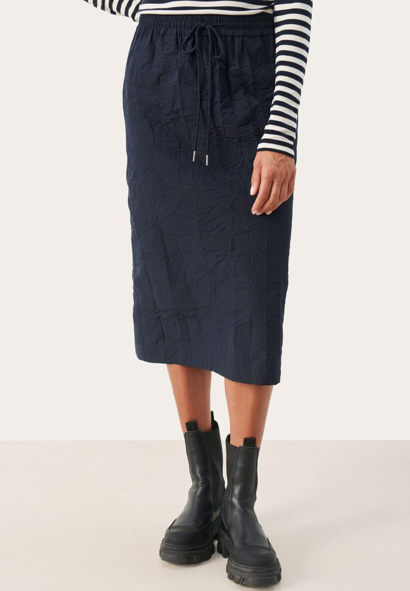 Marineblauwe midi-rok in gekreukt textuur, met een elastische tailleband en een trekkoord, gecombineerd met zwarte enkellaarsjes.