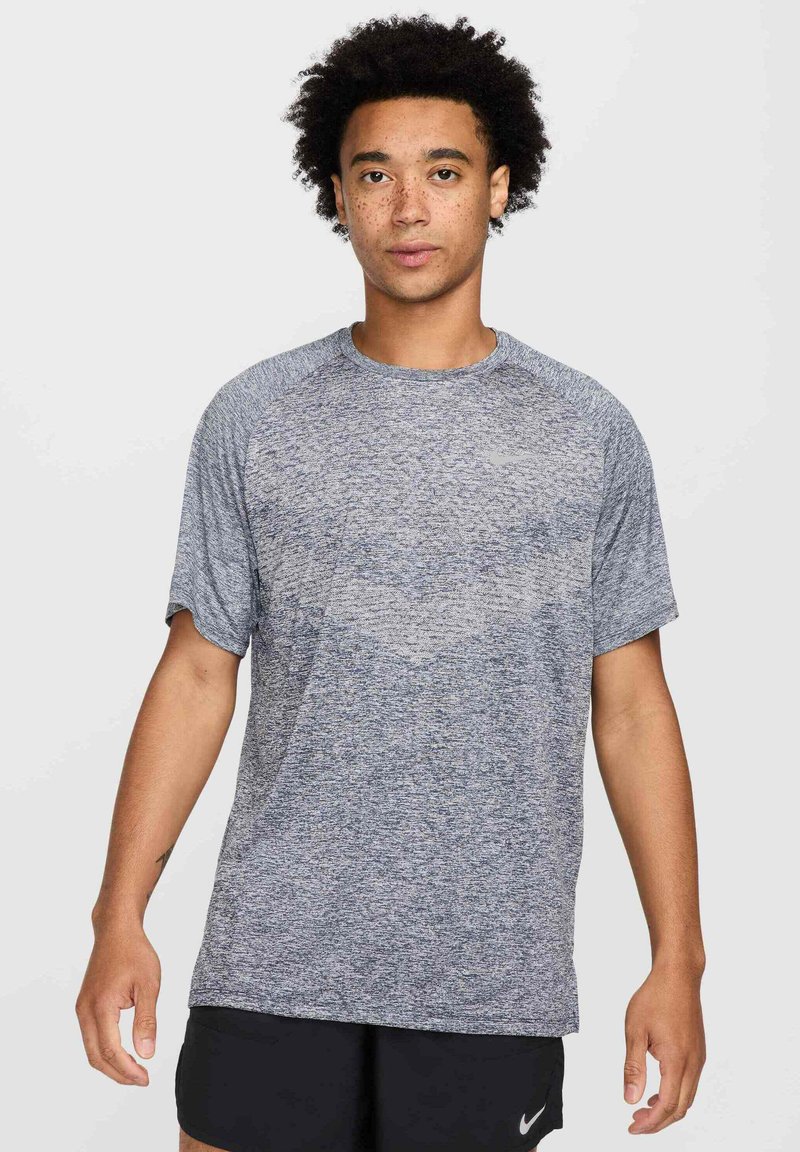 Camiseta atlética de manga corta en gris para hombre, con un patrón texturizado, cuello redondo y corte holgado, combinada con pantalones cortos negros.