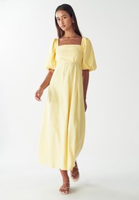Žlté midi šaty s nafúknutými rukávmi a štvorcovým výstrihom, s voľnou sukňou a mäkkou, textúrovanou tkaninou.