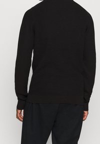 Tumma ruskea neulepusero, jossa on teksturoitu kuvio, pitkät hihat ja rento istuvuus. Resorireunukset hihansuissa ja helmassa antavat ryhdikkyyttä.