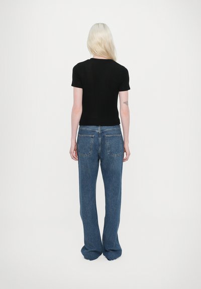 Camicetta nera a maniche corte abbinata a jeans larghi azzurri. Il tessuto appare liscio con uno stile classico e dettagli minimi.