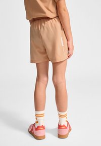 Pfirsichfarbene Shorts mit einem elastischen Bund und weißem "hummel"-Logo an der Seite. Kombiniert mit pinken Schuhen und gestreiften Socken.