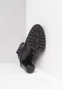 Czarny skórzany botek do kostki z wąskim obcasem, teksturowaną gumową podeszwą z wzorzystym bieżnikiem oraz bocznym zamkiem.